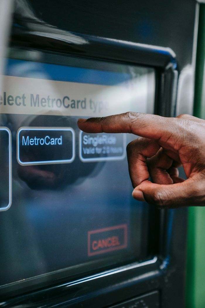 Close-up of a hand using a MetroCard payment touchscreen for subway access.